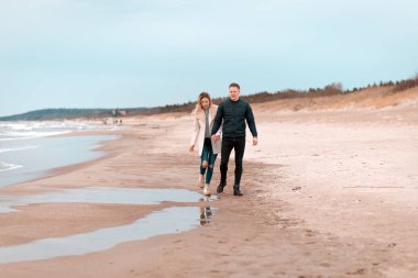 İlkbahar romantik tatilinde kumlu bir plajda, açık havada yürüyen çekici genç bir çift. Seyahat eden turistlerin yaşam tarzı. Çiftler birlikte eğleniyorlar..