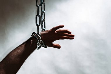 Zincirli el, yukarıdan sarkan zincir. Gri arka plan. Uzayı kopyala, seçici odaklanma..