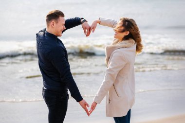 İlkbahar, sonbahar akşamları, deniz kıyısında kollarıyla kalp şeklinde kalp yapan genç çift. Elleriyle plajda kalp şekli oluşturan mutlu çift..