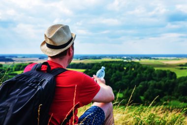 Gezgin dağlarda su içiyor. Sırt çantalı gezgin dağın tepesinde dinleniyor ve güneşli yaz gününde şişe su içiyor..