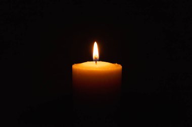 Siyah arkaplanda parlak bir mum yanıyor. Sarı mum alevi. Karanlıktaki mum alevi. Uzayı kopyala..