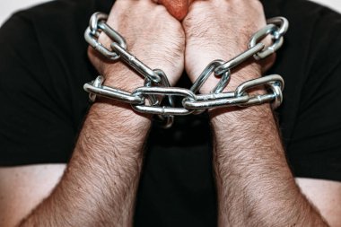 elleri zincirli depresif bir adam. İki eli demir zincirli. Gri arka plan, seçici odaklanma..