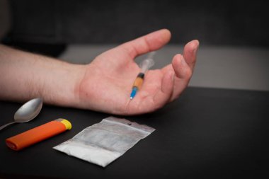 Karanlık odada elinde şırıngayla uyuşturucu dolu bir çanta, bir kaşık ve çakmakla uyuşturucu bağımlısı bir el..