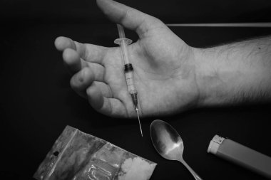 Karanlık odada elinde şırıngayla uyuşturucu dolu bir çanta, bir kaşık ve çakmakla uyuşturucu bağımlısı bir el..