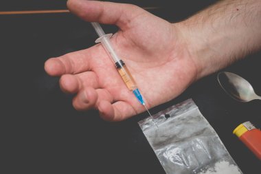 Karanlık odada elinde şırıngayla uyuşturucu dolu bir çanta, bir kaşık ve çakmakla uyuşturucu bağımlısı bir el..