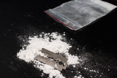 Uyuşturucu barutu üzerinde jilet, siyah arka planda kokain torbası. Boşluğu kopyala..