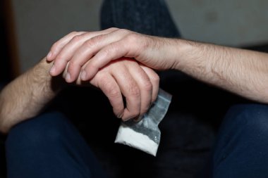 Uyuşturucu dolu plastik poşet taşıyan bir suçlu. Elinde şeffaf plastik bir torba tutan bir adam. Uyuşturuculu kavramsal suçlu. Yakından, seçici odaklı, uyumlu..