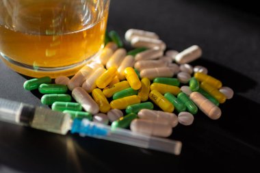 Koyu gri masada sert uyuşturucu ve alkol. Alkol hapları. Plastik kokain torbası. Masada gölgeli..