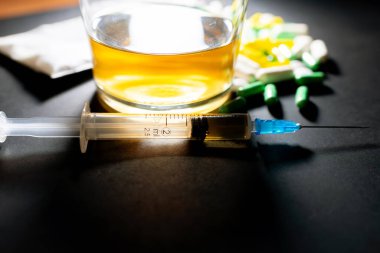 Koyu gri masada sert uyuşturucu ve alkol. Alkol hapları. Plastik kokain torbası. Masada gölgeli..
