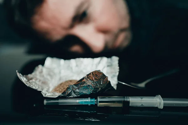 薬の注射器と火の上のヘロイン 男は薬を見るために頭を傾けた 反射と黒のテーブル — ストック写真