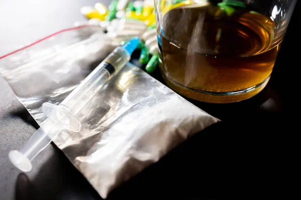 濃い灰色のテーブルの上にハードドラッグとアルコール アルコール錠剤は 影とテーブルの上にコカインのビニール袋の粉を注射します — ストック写真
