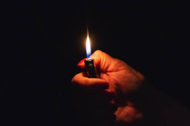 Karanlık arka planda yanan bir çakmak tutan bir kadın. Yaklaş, seçici odaklan. Boşluğu kopyala.
