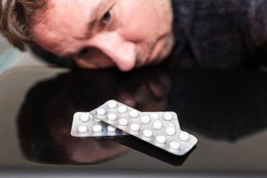 Uyuşturucu bağımlısı beyaz ilaç haplarını siyah masaya yansıtmış. Adam haplara bakmak için başını eğmiş..