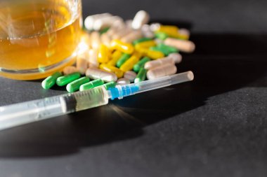 Koyu gri masada sert uyuşturucu ve alkol. Alkol hapları. Plastik kokain torbası. Masada gölgeli..