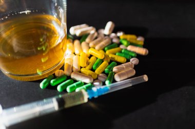 Koyu gri masada sert uyuşturucu ve alkol. Alkol hapları. Plastik kokain torbası. Masada gölgeli..