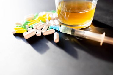 Koyu gri masada sert uyuşturucu ve alkol. Alkol hapları. Plastik kokain torbası. Masada gölgeli..