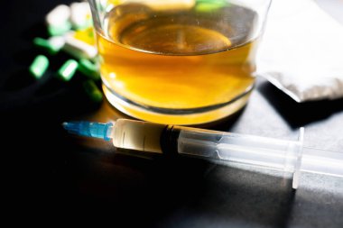 Koyu gri masada sert uyuşturucu ve alkol. Alkol hapları. Plastik kokain torbası. Masada gölgeli..