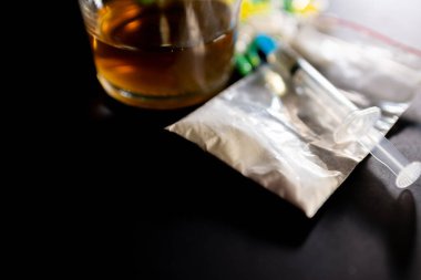 Koyu gri masada sert uyuşturucu ve alkol. Alkol hapları. Plastik kokain torbası. Masada gölgeli..