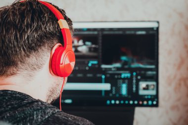 Adam kulaklık takıyor, profesyonel bilgisayarda film kurguluyor, masa.video düzenleyicisi yeni bir film projesi başlatıyor, sesli film montajı. Arka plan, yakın plan, seçici odaklanma..