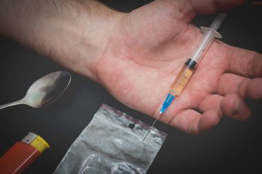 Karanlık odada elinde şırıngayla uyuşturucu dolu bir çanta, bir kaşık ve çakmakla uyuşturucu bağımlısı bir el..