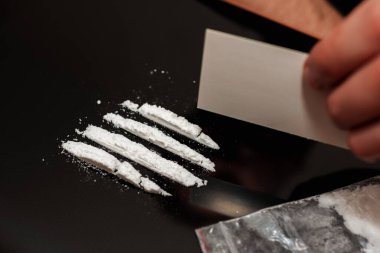 Bağımlı, kokainin izini sürüyor. Bağımlı uyuşturucu kullanıcısı, siyah aynada beyaz toz çizgileri çiziyor. Yakından..