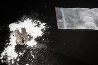 Uyuşturucu barutu üzerinde jilet, siyah arka planda kokain torbası. Boşluğu kopyala..