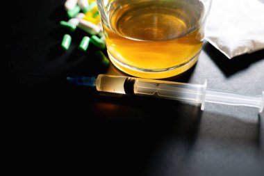 Koyu gri masada sert uyuşturucu ve alkol. Alkol hapları. Plastik kokain torbası. Masada gölgeli..