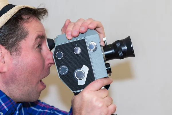 驚きの男は灰色の背景にヴィンテージ映画カメラを保持します 男はホームムービーを撮影します フィルムカメラに選択的な焦点 クローズアップ コピースペース サイドビュー 屋内で撮影 — ストック写真