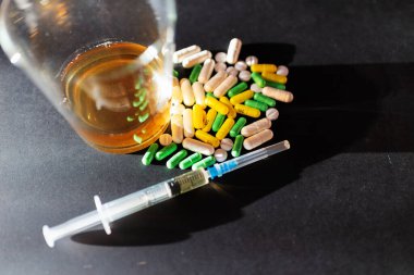 Koyu gri masada sert uyuşturucu ve alkol. Alkol hapları. Plastik kokain torbası. Masada gölgeli..