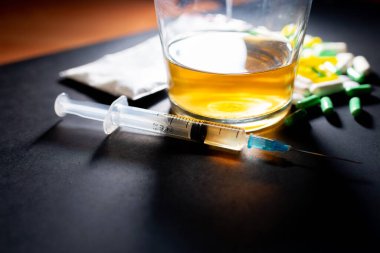 Koyu gri masada sert uyuşturucu ve alkol. Alkol hapları. Plastik kokain torbası. Masada gölgeli..