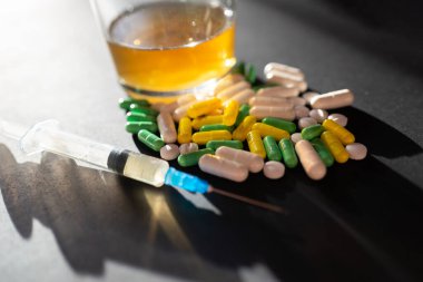 Koyu gri masada sert uyuşturucu ve alkol. Alkol hapları. Plastik kokain torbası. Masada gölgeli..