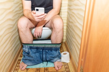 Tuvalette otururken akıllı telefon kullanan ve cep telefonuyla mesajlaşan bir adam. Sağlıklı bir kavram..