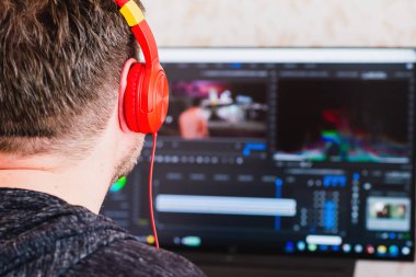 Evde çalışırken kulaklık takan Freelancer, post prodüksiyon yazılımını kullanarak video düzenliyor. Videograf, film kurgusunu bilgisayarda işliyor. Seçici odak, arka görünüm, boşluğu kopyala.