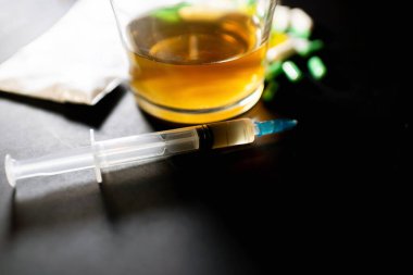 Koyu gri masada sert uyuşturucu ve alkol. Alkol hapları. Plastik kokain torbası. Masada gölgeli..