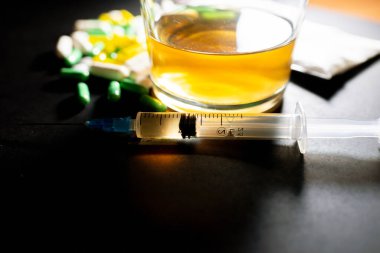 Koyu gri masada sert uyuşturucu ve alkol. Alkol hapları. Plastik kokain torbası. Masada gölgeli..