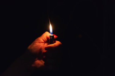 Karanlık arka planda yanan bir çakmak tutan bir kadın. Yaklaş, seçici odaklan. Boşluğu kopyala.