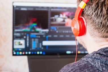 Kulaklıklı bir adam, profesyonel bilgisayarda film kurgusu yapıyor. Freelancer video editörü, film projesi ses filmi montajı yapıyor. Arka plan, yakın plan, seçici odaklanma..