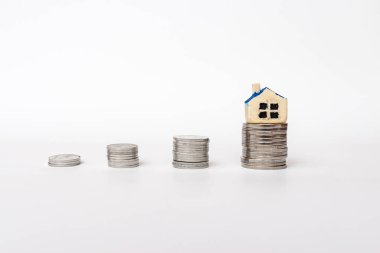 Beyaz arka planda dört yığın para. Üst sütundaki minyatür oyuncak evi. Boşluğu kopyala.