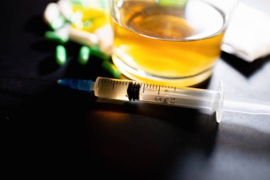 Koyu gri masada sert uyuşturucu ve alkol. Alkol hapları. Plastik kokain torbası. Masada gölgeli..