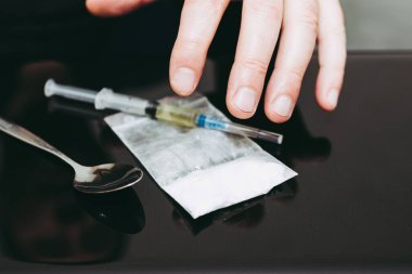 Narkotik uyuşturucu şırıngası, kaşık, torba ve kokain ya da masanın üzerinde eroin. Arka plandaki adamın eli bulanık..