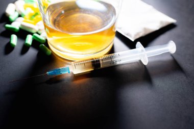 Koyu gri masada sert uyuşturucu ve alkol. Alkol hapları. Plastik kokain torbası. Masada gölgeli..
