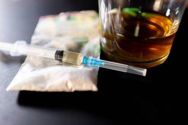 Koyu gri masada sert uyuşturucu ve alkol. Alkol hapları. Plastik kokain torbası. Masada gölgeli..