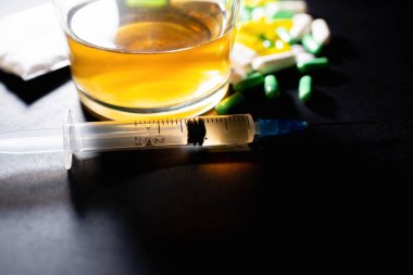 Koyu gri masada sert uyuşturucu ve alkol. Alkol hapları. Plastik kokain torbası. Masada gölgeli..