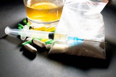 Koyu gri masada sert uyuşturucu ve alkol. Alkol hapları. Plastik kokain torbası. Masada gölgeli..