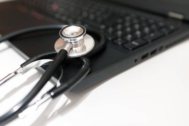 Stetoskop ve dizüstü bilgisayarı olan bir doktor işyeri. Tıbbi teknoloji geçmişi, doktorun steteskopu ve dizüstü bilgisayarı üzerine seçici odaklanma, siyah ve beyaz. Çevrimiçi sağlık, teletıp kavramı. Kapatın.