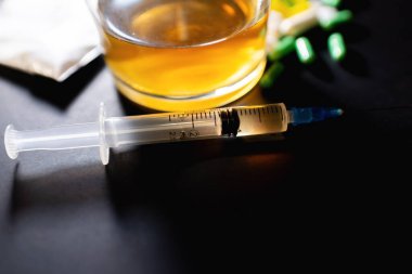Koyu gri masada sert uyuşturucu ve alkol. Alkol hapları. Plastik kokain torbası. Masada gölgeli..