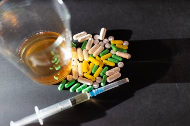 Koyu gri masada sert uyuşturucu ve alkol. Alkol hapları. Plastik kokain torbası. Masada gölgeli..