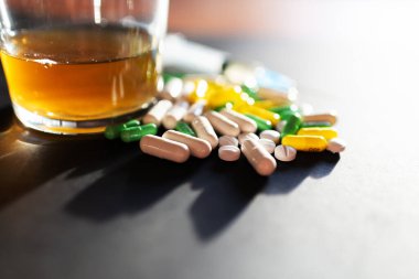 Koyu gri masada sert uyuşturucu ve alkol. Alkol hapları. Plastik kokain torbası. Masada gölgeli..