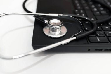 Stetoskop ve dizüstü bilgisayarı olan bir doktor işyeri. Tıbbi teknoloji geçmişi, doktorun steteskopu ve dizüstü bilgisayarı üzerine seçici odaklanma, siyah ve beyaz. Çevrimiçi sağlık, teletıp kavramı. Kapatın.