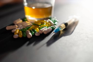 Koyu gri masada sert uyuşturucu ve alkol. Alkol hapları. Plastik kokain torbası. Masada gölgeli..